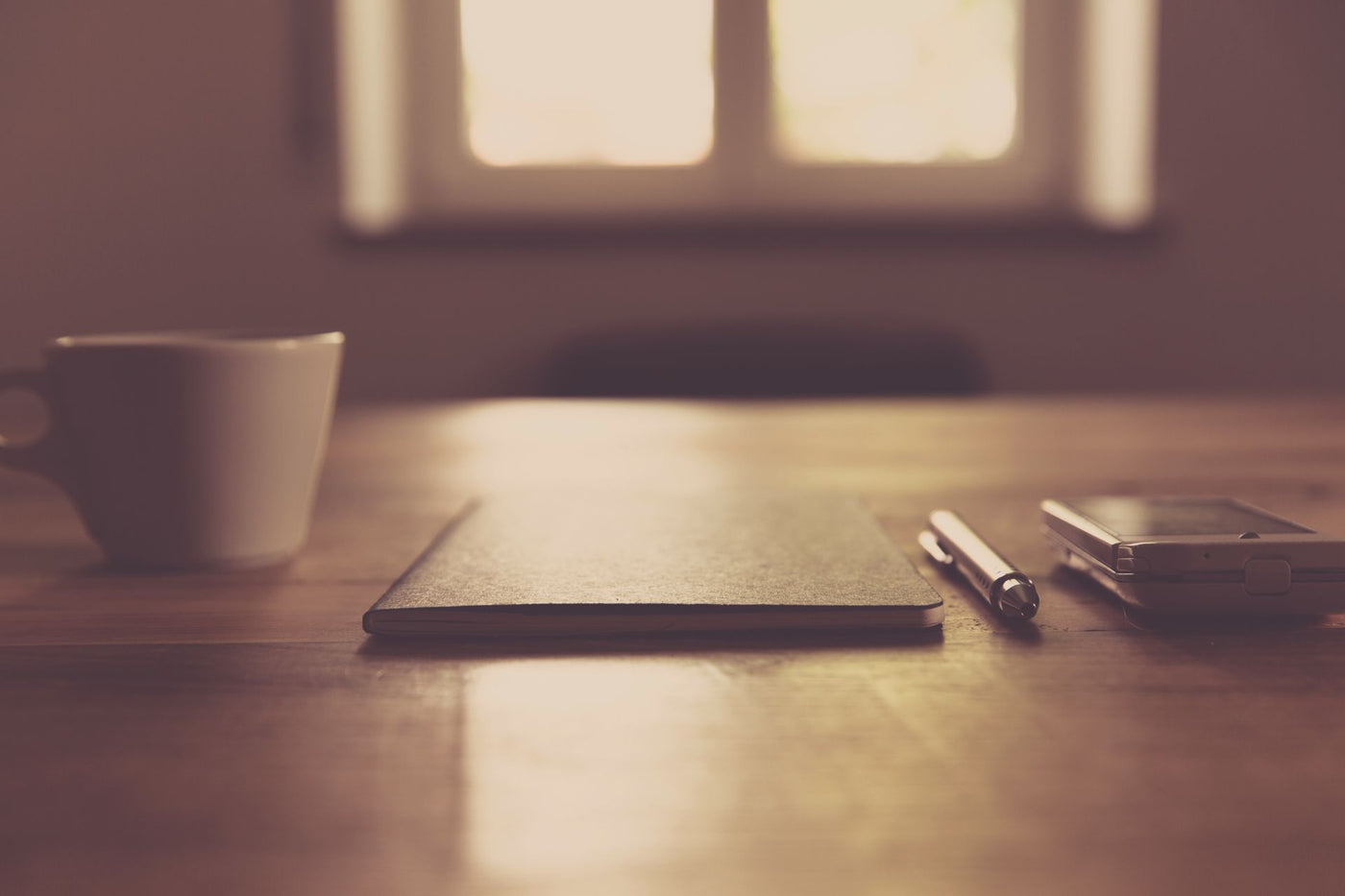A coffee cup and notebook on a wooden desk in warm afternoon window light