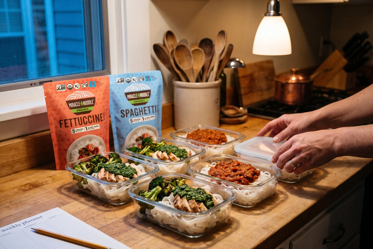 Hands sealing glass meal-prep containers of white konjac noodles with chicken, broccoli and ragu, with Miracle Noodle Fettuccine and Spaghetti pouches on the counter
