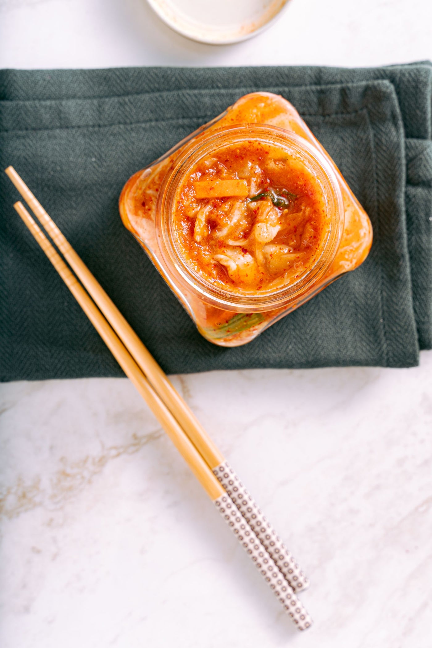 A jar of homemade kimchi with chopsticks on a green cloth