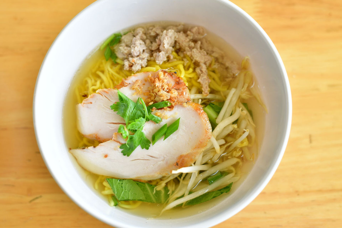 A noodle bowl with fresh herbs in a white bowl on a light wooden table