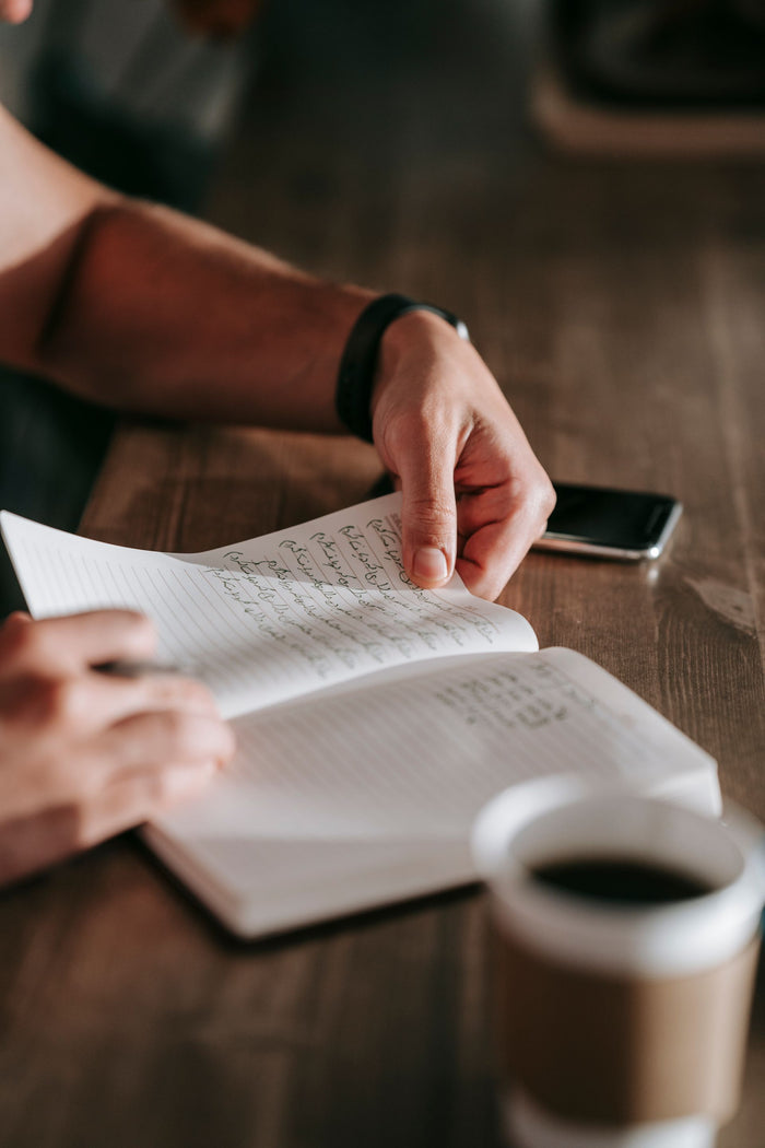 A person paging back through a handwritten journal beside a cup of coffee