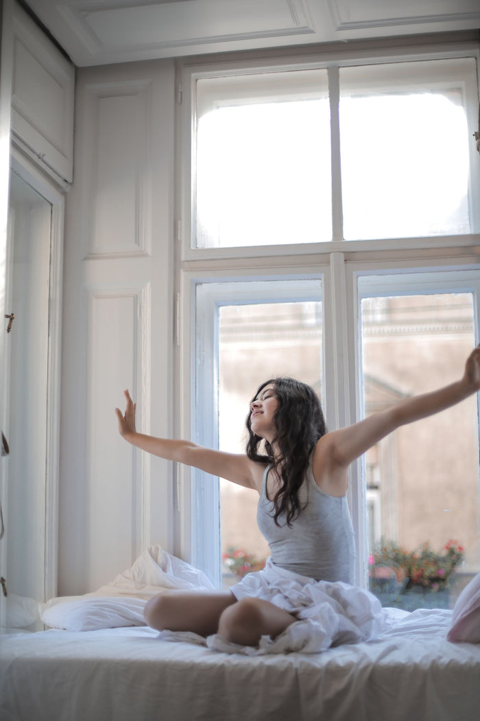 A woman stretching as she wakes in soft morning window light