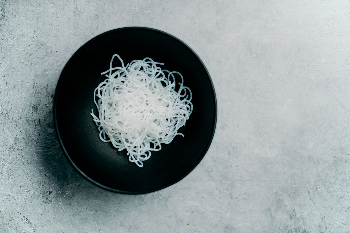 A nest of white konjac-style noodles in a dark ceramic bowl, seen from above