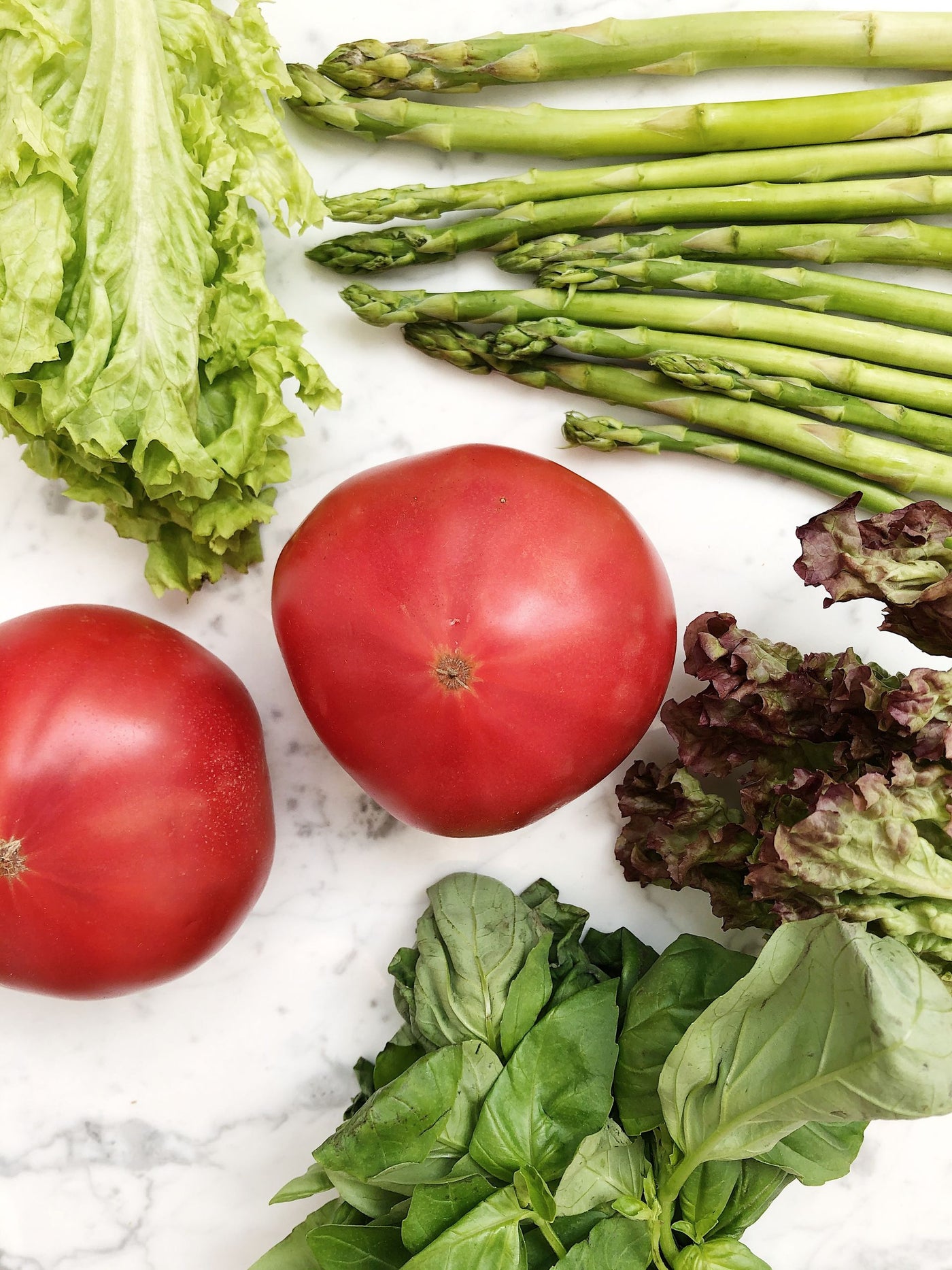 Fresh vegetables — lettuce, asparagus, tomatoes, and basil laid out on a marble counter