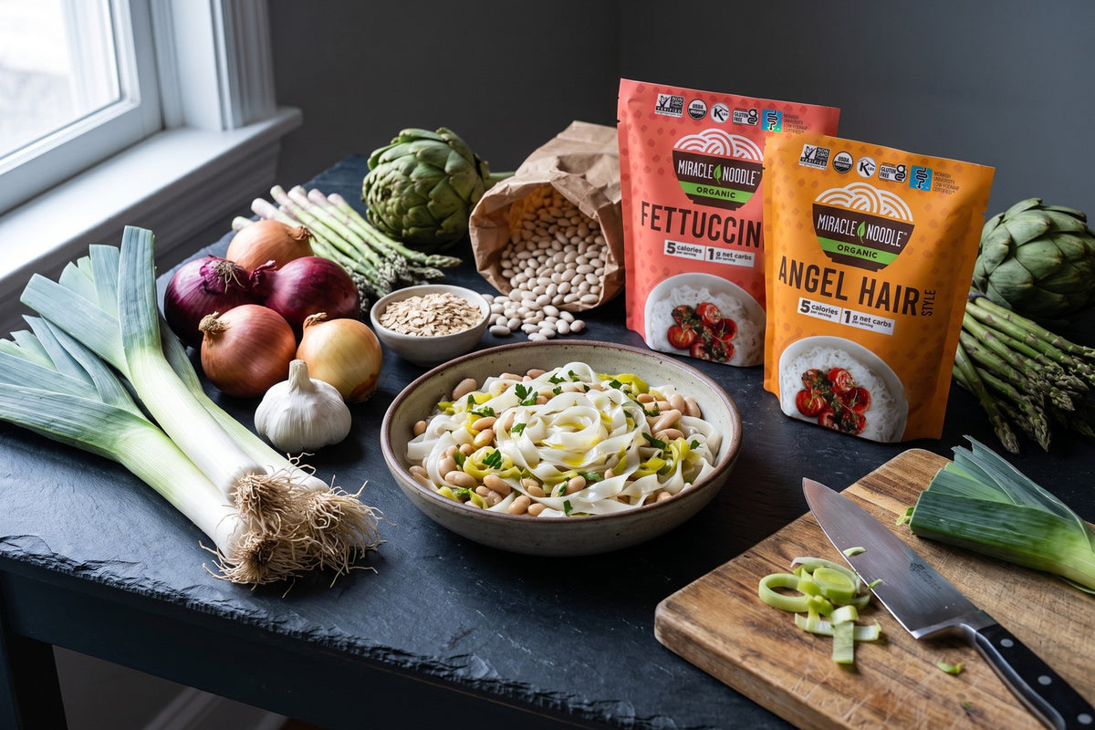 Leeks, onions, garlic, asparagus, artichokes and white beans around a bowl of konjac fettuccine with beans and leeks, with Miracle Noodle Fettuccine and Angel Hair pouches